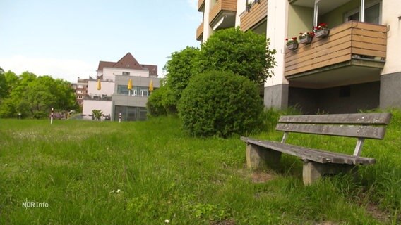 Mehrere Wohngebäude mit Balkonen, im Vordergrund steht eine leere Sitzbank. © Screenshot 
