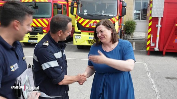 Hamburgs Zweite Bürgermeisterin Katharina Fegebank schüttelt die Hand eines Feuerwehrmannes in Merseille. © Screenshot 