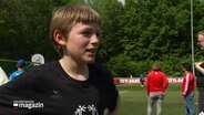 Ein Junge im Interview, im Hintergrund weitere Menschen auf dem Fußballplatz. © Screenshot 