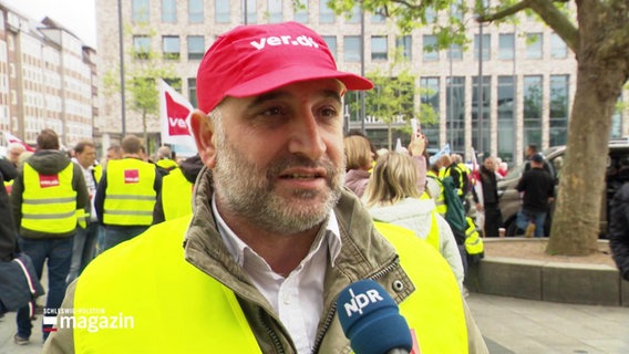 Lagerarbeiter Vanit Aktepe im Interview, im Hintergrund weitere Streikende. © Screenshot 
