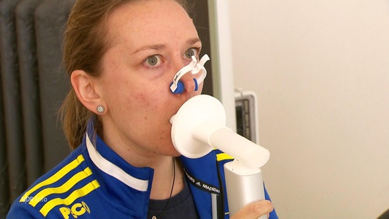 Eine junge Frau Pustet in ein Lungenprüfgerät. © Screenshot 