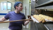 Eine Bäckerin checkt Backware aus dem Ofen. © Screenshot 