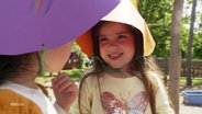 Kinder tragen selbst gebastelte Sonnenhüte aus bunter Pappe. © Screenshot 