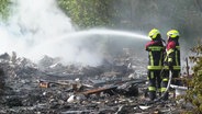 Zwei Feuerwehrleute bei Löscharbeiten an einem abgebrannten Haus. © Screenshot 