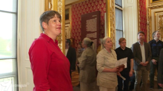 Julia Tackmann führt eine Gruppe von Menschen durch ein Museum. © Screenshot 