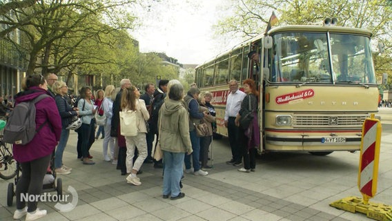 Mehrere Personen stehen vor einem älteren Reisebusmodell zum Einsteigen bereit. © Screenshot 