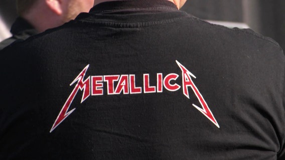 Eine Person trägt ein schwarzes Shirt mit der Aufschrift Metallica auf dem Rücken. © Screenshot 