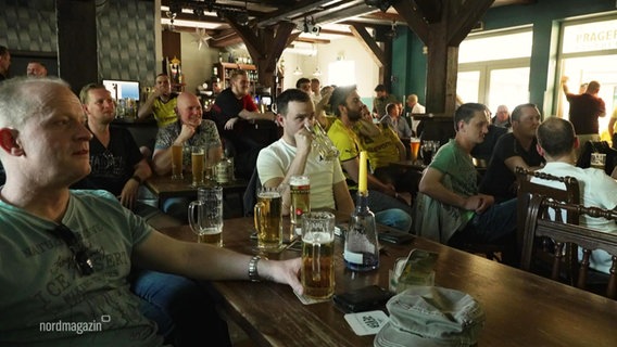 Blick in ein Fußball-Lokal: Viele Dortmund-Fans sitzen bei einem Public Viewing mit Bier gespannt zusammen. © Screenshot 