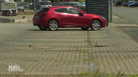Blick auf ein rotes Auto, das auf einem sonst leeren Parkplatz steht. © Screenshot 
