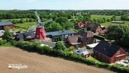 Blick auf Nübbel aus der Luft. Mitten im Ort ragt eine große, rote Windmühle gen Himmel. © Screenshot 