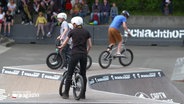 Drei junge Menschen fahren mit ihren BMX-Rädern über die Rampen eines Skateparks. © Screenshot 