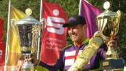 Paul Cooper feiert seinen Sieg beim Bergringrennen mit zwei Pokalen. © Screenshot 