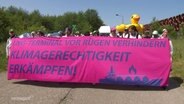 Protestierende halten ein Banner mit der Aufschrift: "LNG-Terminal von Rügen verhindern - Klimagerechtigkeit Erkämpfen!" © Screenshot 