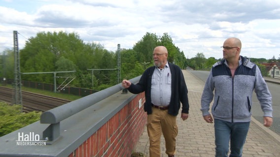 Zwei Männer auf einer Brücke über Bahngleisen. © Screenshot 
