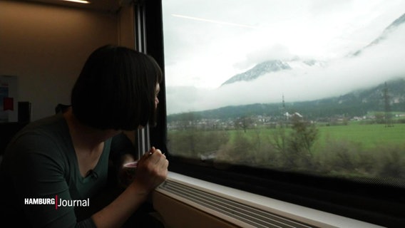 Eine Frau blickt durch ein Zugfenster auf ein Bergpanorama. © Screenshot 