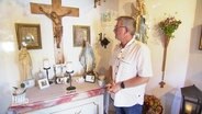 Udo Bauch, Überlebender des Zugunglücks von Eschede, steht vor einem Altar mit Kreuz. © Screenshot 