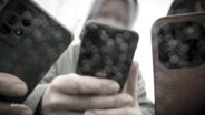 Nahaufnahme von drei nicht-erkennbaren Personen, die ihre Smartphones zum Fillmen in die Kamera halten. © Screenshot 