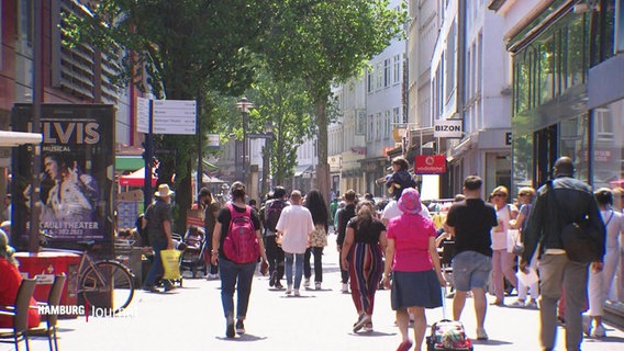 Blick in eine Fußgängerzone einer Einkaufsstraße: Viele Menschen flanieren an einem sonnigen Tag an Geschäftszeilen vorbei. © Screenshot 