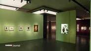 Blick in eine Kunstausstellung: An grünen Wänden hängen mehrere eingerahmte Fotografien. © Screenshot 