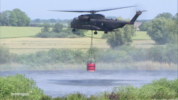 Ein Militärhubschrauber holt Löschwasser aus einem See. © Screenshot 