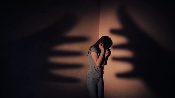Eine Person steht in der Ecke eines Raumes, die Schatten zweier Hände greifen nach ihr. © Screenshot 