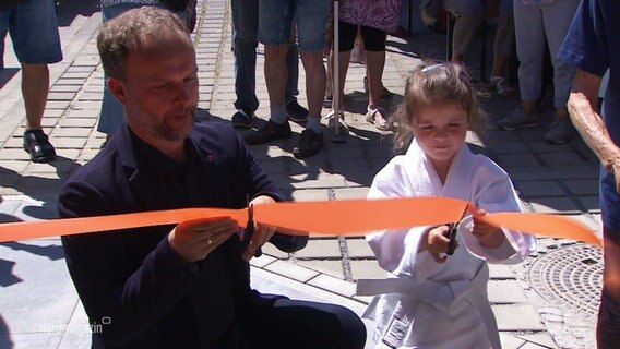 Ein Mädchen in Judo-Kleidung zerschneidet ein totes Band. © Screenshot 