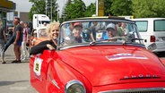 Menschen sitzen in einem roten Oldtimer Cabrio. © Screenshot 