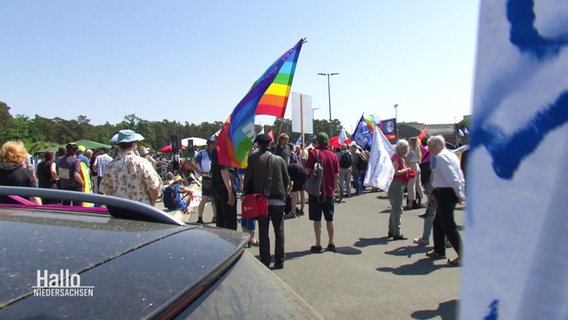 Mehrere Menschen stehen bei einer Demonstration mit bunten Fahnen und Transparenten versammelt auf einem Platz. © Screenshot 