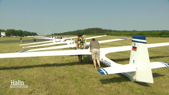 Mehrere Personen schieben ihre Segelflugzeuge in einer Schlange vor der Startbahn auf Position. © Screenshot 