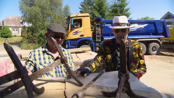 Abrissunternehmer Roberto Lenuweit steht im bunten Anzug beratend mit einem Bauleiter auf einer Baustelle zusammen. © Screenshot 