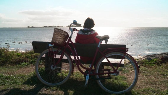 Heike Götz mit Fahrrad auf einer Bank an der Ostsee im Gegenlicht © Screenshot 