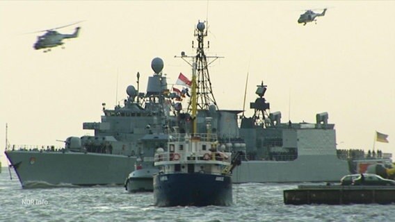 Ein Kriegsschiff und mehrere kleine (zivile) Boote tümmeln sich auf einem Gewässer. © Screenshot 