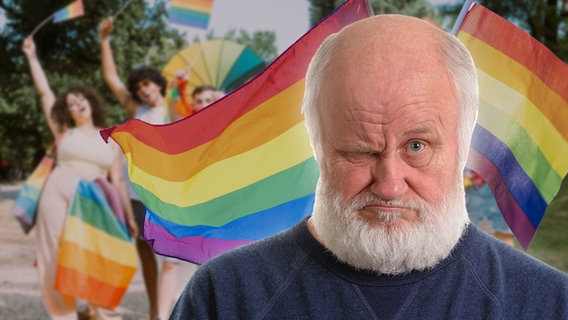 Ein grimmig schauender Mann vor einer Regenbogenfahne. (extra 3 vom 15.06.2023 im Ersten) © NDR 