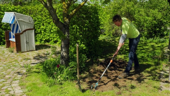 Ein Gärtner bearbeitet den Boden mit einer Harke. © Screenshot 