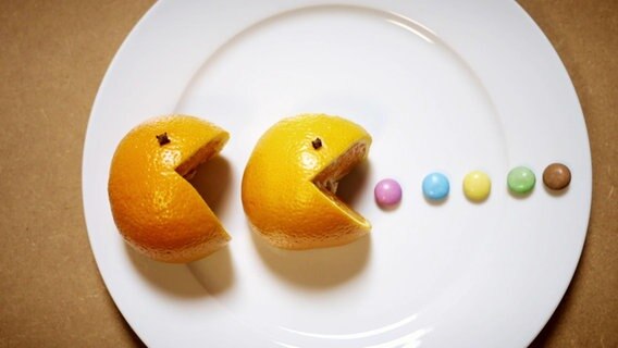 Zwei Orangen, aussehend wie die Figur Pac-Man, essen bunte Schokolinsen. © Screenshot 