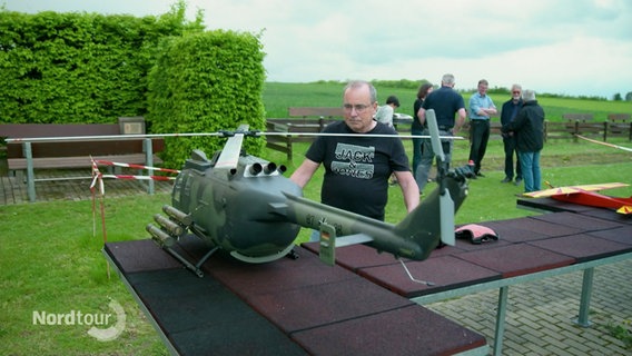 Ein Mann begutachtet ein auf einem Tisch stehendes, größeres Modell eines Militärhubschraubers. © Screenshot 