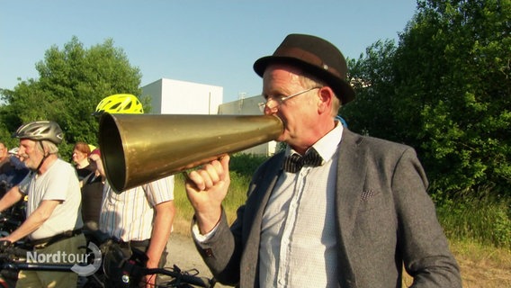 Ein älterer Mann spricht durch eine Flüstertüte aus Blech. © Screenshot 