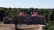 Blick aus der Vogelperspektive: Ein älteres Herrenhaus-Gebäude steht vor einem Waldstück. © Screenshot 