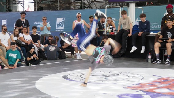 Ein junger Breakdancer im einhändigen Handstand auf einer Bühne vor Publikum © Screenshot 