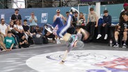Ein junger Breakdancer im einhändigen Handstand auf einer Bühne vor Publikum © Screenshot 