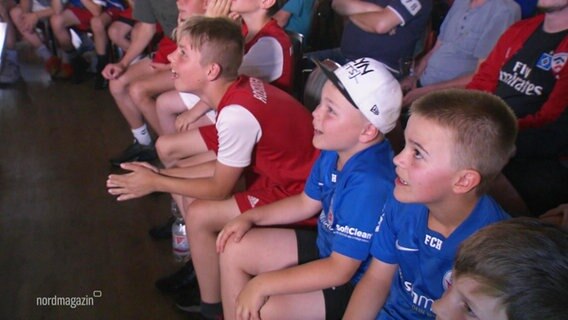 Mehrere Kinder in Fussballtrikots sitzen nebeneinander. © Screenshot 