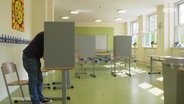 Ein Bürger hinter einer Wahlkabine bei einem Bürgerentscheid. © Screenshot 