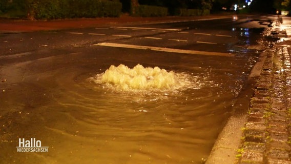Wasser tritt aus einem Gullideckel einer überschwemmten Straße. © Screenshot 