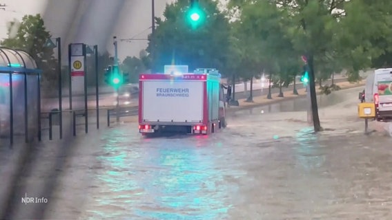 Ein Feuerwehrauto kämpft sich durch Wassermassen auf einer Straße in Braunschweig. © Screenshot 