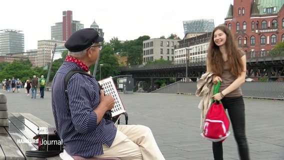 Straßenmusiker mit Akkordeon sitzt am Straßenrand bei den Landungsbrücken. © Screenshot 
