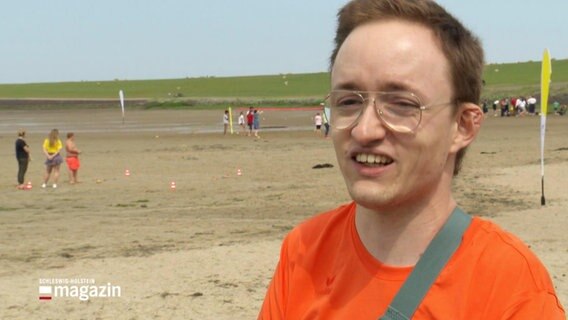 Auf dem Bild sieht man Tyll Reinisch - Inklusionsmanager. Er steht auf der rechten Seite des Fotos und trägt ein orangenes T-Shirt. © Screenshot 