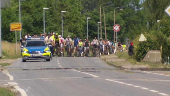 Viele Radfahrende fahren hinter einem Polizeiauto auf einer Straße. © Screenshot 