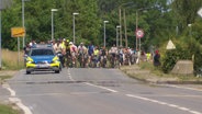 Viele Radfahrende fahren hinter einem Polizeiauto auf einer Straße. © Screenshot 