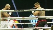 Zwei Boxer stehen mit erhobenen Fäusten sich gegenüber bei einem Kamp in einem Ring. © Screenshot 