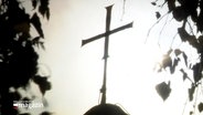 Das Kreuz der Kirche steht auf einem Kirchendach. © Screenshot 